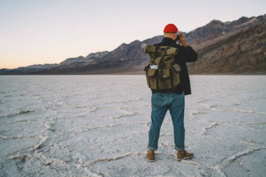 Sırt çantalı erkek turistin, hafta sonunu Badwater Havzası 'nda geçirirken kurak arazide dağların fotoğrafını çekerken görüntüsü.