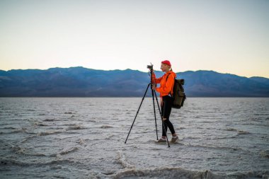 ABD 'de zaman geçirirken, dağlarla birlikte kuru arazi manzarası çekmek için fotoğraf makinesi kullanan kadın sırt çantasının yan görüntüsü.