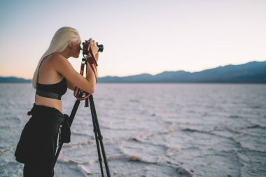 Yaz aylarında Badwater Havzası 'nda vakit geçirirken gün batımının altında dağlık arazinin fotoğraflarını çeken genç bayan yolcuların yan görüntüsü.