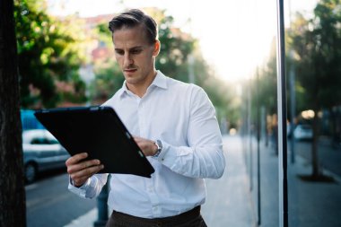 Genç Kafkasyalı işadamı şehir merkezindeki 4g internet bağlantısını kullanarak bankacılık işlemlerini kontrol ediyor, milenyum girişimcisi sokak kentleşmesinde ayakta duran web yayınını okuyor