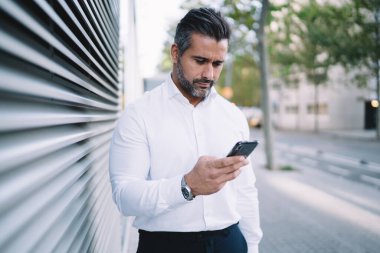 Başarılı erkek girişimci i-beyaz gömlekli. Hesap bakiyesi için cep telefonu uygulaması kullanıyor. Kafkas işadamı iş arkadaşlarıyla mesajlaşıyor.