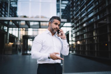 Ciddi bir erkek çalışan şirket detaylarını konuşmak için operatör ile iletişim kuruyor cep telefonu uygulamasını açık havada kullanıyor, olgun bir işadamı ortağına telefon ediyor gezgin internet bağlantısını kullanıyor.