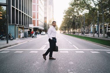 Şehir merkezinde beyaz gömlekli beyaz iş adamının tam boy portresi. Kameraya bakıyor. Elinde evrak çantası olan olgun bir bankacı.