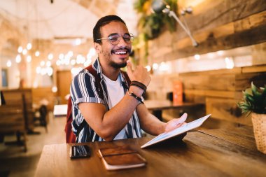 Modern dijital tablet kullanan mutlu koyu tenli erkek öğrenci aletler ve 4G bağlantısıyla tatmin olmuş, Afro-Amerikan milenyum blogcusu serbest çalışmanın tadını çıkarıyor.