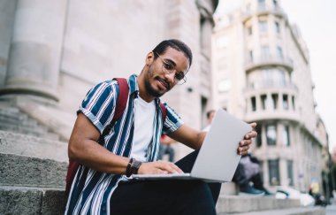 Gözlüklü genç bir adamın merdivenlerde oturup kameraya bakarken netbook 'a bakmasından.