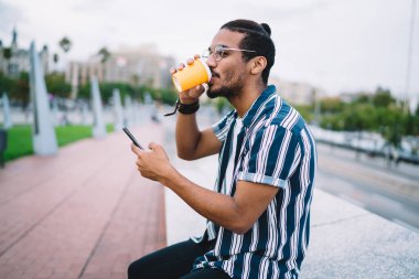 Yakışıklı, koyu tenli hippi, sokakta oturmuş kahve içiyor ve akıllı telefondan mesaj yolluyor. Milenyum erkek blogcu, hafta sonları şehirdeki cep telefonundan bildirimi kontrol ediyor.