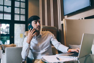 Laptop bilgisayarında yazan kendinden emin erkek girişimci akıllı telefon görüşmesi yapıyor çevrimiçi geliri tartışıyor, gururlu müreffeh Latin adam ceo modern teknolojileri kullanarak modern iç mekanlarda uzak iş yapıyor.