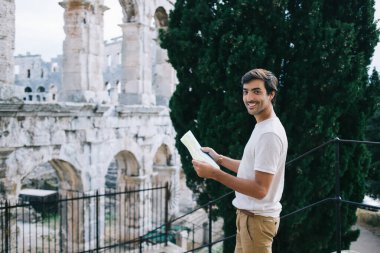 İtalya 'daki antik Kolezyum' da kağıt haritaya bakarken kameraya gülümseyen yetişkin ve memnun bir adamın yüksek açılı yan görüntüsü.