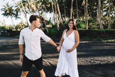 Yeşil parkta dikilen, gülümseyen ve güneşli bir günde eğlenen şık elbiseli mutlu çift.