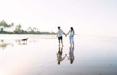 Beyaz elbiseli, isimsiz bir çift gölün ıslak sahillerinde yürüyor ve yalnız köpeğe bakarken el ele tutuşuyorlar.
