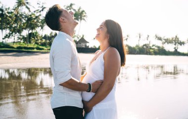 İyimser genç çift, güneşli bir günde kumsalda birlikte vakit geçirirken birbirlerine gülüp sarılıyorlar.