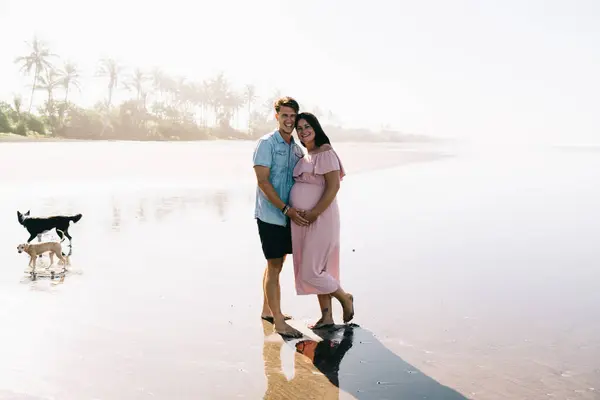 Full body man and pregnant woman in casual wear standing and hugging while enjoying stroll on water during weekend on sunny day