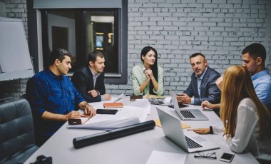 Masa başında oturan ve proje taslaklarını analiz eden resmi giyimli deneyimli erkek ve kadın meslektaşlardan oluşan bir grup. Ofisteki başlangıç projesinde işbirliği yapan profesyonel mimarlar.