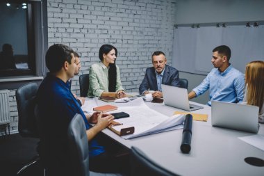 Masa başında oturan ve proje taslaklarını analiz eden resmi giyimli deneyimli erkek ve kadın meslektaşlardan oluşan bir grup. Ofisteki başlangıç projesinde işbirliği yapan profesyonel mimarlar.