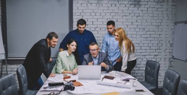 Deneyimli tasarımcılar, online çizimler ve proje planları için modern dizüstü bilgisayar kullanıyorlar, masa başında netbook ve planlarla işbirliği yapan yetenekli mimarlar grubu