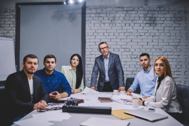 Planlar ve takım oluşturma konsepti için yapılan beyin fırtınası sırasında ofis masasında poz veren başarılı bir çalışan ekibiyle resmi olarak giyinmiş erkek şirket yöneticisinin portresi.