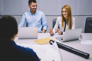 Erkek ve kadın meslektaşlar, ofis içi çalışma günlerinde eskiz ve plan analizi yapıyor. Masaüstünde oturuyor ve ticaret değiş tokuşu, başarılı şirket yöneticileri brifingi hakkında iletişim kuruyor.