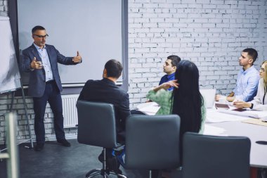 Resmi olarak giyinmiş ofis çalışanları iş projesinde işbirliği yapıyor şirket yönetim kurulu odasında konuşuyor, olgun yönetici firmada beyin fırtınası sırasında deneyim paylaşımı yapıyor