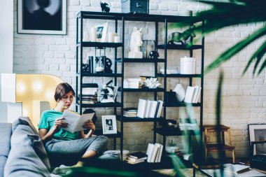 Yoğunlaşmış kadın edebiyat entrikaları okuyor. Haftasonunu şık iç mekanlarda okumak için harcıyor. Optik gözlüklü beyaz kız, en çok satanlarla ilgileniyor.