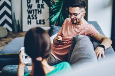 Optik gözlüklü neşeli hippi kız arkadaşıyla hafta sonunun keyfini çıkarıyor. Cep telefonu aygıtını kullanarak online rezervasyon durumunu kontrol ediyor. Mutlu çift evde iletişim kuruyor.