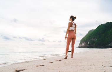 Beyaz bluzlu anonim bir kadın ve kumlu deniz kıyısında bulutlu gökyüzüne bakarken tozlukların arkası.