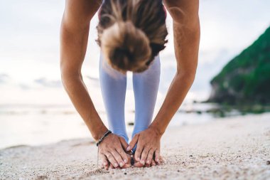 Çıplak ayaklı, bileklerinde topuz ve bilekliği olan, Uttanasana yoga pozu veren, Bali 'deki kumlu plajda çıplak ayaklı bir kadın.