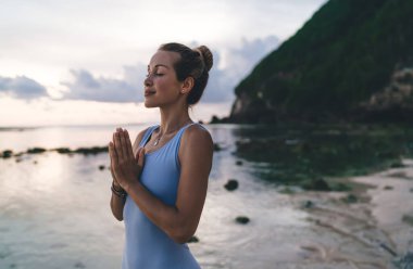 Spor eşofmanlı sakin genç bir kadın akşam vakti kıyı sporu için harmoni egzersizleri yapıyor namaste 'de yoga antrenmanından keyif alan Kafkasyalı sakin bir bayan sporcu.