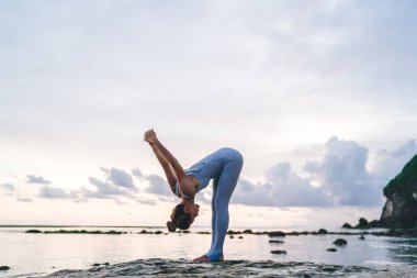 Spor kıyafetleri içinde kadın vücudunun yan görüntüsü bilek kilidi tutamağı ile el ele tutuşup Bali sahilinde dizlerini bükerken.