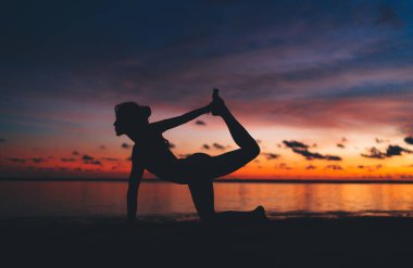 Tanınmayan bir kadın silueti dizlerinin üzerinde duruyor ve kıyı şeridinde bacağını kaldırıyor. Bu arada Half Bow asana 'yı muhteşem günbatımı manzarasının arka planında yapıyor.