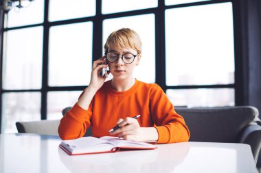 Masada oturup not defterine notlar yazan ciddi bir serbest çalışan kadın yeni bir proje üzerinde çalışırken cep telefonuyla sohbet ediyor.