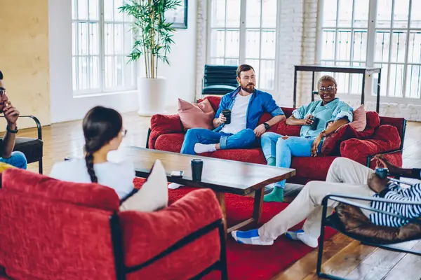 Diverse young people discussing taste of caffeine beverage having friendly meeting in cozy loft apartment, multicultural best friends 20s talking during rest weekend for socialising at home