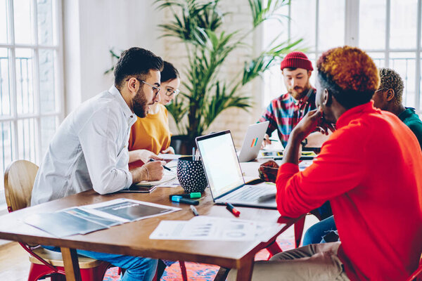 Diverse male and female creative colleagues discussing ideas during brainstorming collaborative meeting in coworking,people making research for business project using blank laptop with copy space area