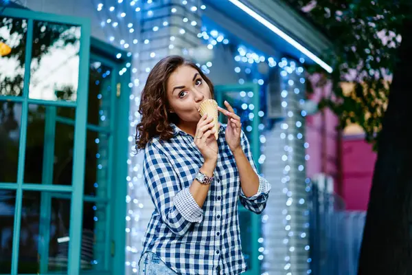 Beautiful Caucasian female in casual shirt eating tasty sweet sorbet dessert in cone waffle enjoying summer weekend in city, young hipster girl taste gelato ice cream during travel vacations