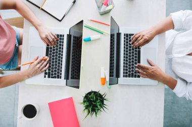 Aydınlık ofiste çalışırken dizüstü bilgisayarlarda yazan, resmi ve günlük giysiler içinde iki farklı isimsiz kadın işçinin...