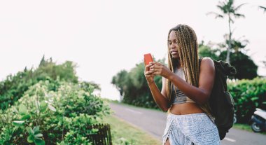 Milenyum hippi kızı macera için boş zamanlarında içerik kontrol metni almış. Sırt çantalı koyu tenli turist seyahat sırasında internet kullanıyor.