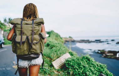 Sırt çantalı Afrikalı Amerikalı kadın turistin tropikal adada yaz macerası boyunca doğa koşullarını araştırması. Açık hava sırt çantalı koyu tenli aktif kadın.
