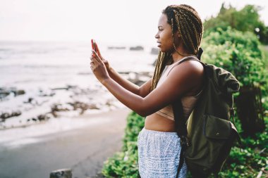 Sırt çantalı koyu tenli gezgin akıllı telefon cihazıyla çevre fotoğrafları çekiyor. Gezide 4G 'ye bağlanan mobil teknolojiyle fotoğraf çeken bin yıllık turist.