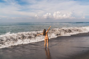 Maldivler 'in kumlu sahillerinde ellerini sallayarak özgürlüğün tadını çıkaran, bikinili, isimsiz bir kadının arka görüntüsü.