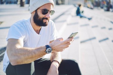 Gezici uygulama üzerinden seyahat yayınını paylaşmak için 4G kablosuz bağlantı kuran Ortadoğulu blogcu, akıllı telefon teknolojisi ile sohbet eden milenyum sakallı adam web uygulaması yüklemek için arama yapıyor
