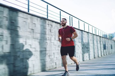 Spor ayakkabılarıyla koşan, kulaklıkla müzik dinleyen, gözlerini kaçıran ve güneşli yazın tadını çıkaran genç bir adam.