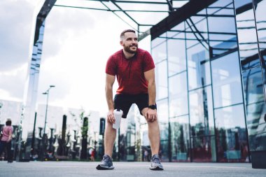 Camdan binaların yanında antrenman yaptıktan sonra şişeyle gezen ve şehirde vakit geçirirken gözlerini kaçıran sporcu.