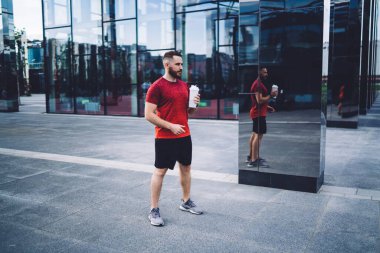 Bir şişe suyla uzun boylu bir erkek sporcu şehir merkezinde duruyor ve koşudan sonra dinlenirken kafasını çeviriyor.