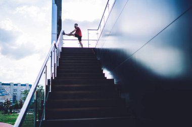 Spor kıyafetli isimsiz bir adamın merdivenlerde durup hava bulutlu olmasına rağmen antrenmandan önce esneme egzersizleri yapmasından.