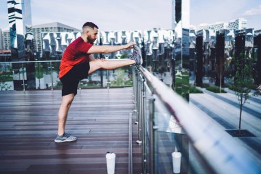 Modern binalara karşı ahşap zeminde pratik yapmadan önce spor ayakkabıları ile koşan erkek koşucunun yan görüntüsü.