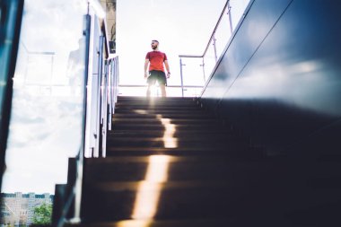 Güneşli bir günde spor yapmaya başlamadan önce merdivenlerin yanında durup bakışlarını kaçıran isimsiz bir adamın alçak açısı.