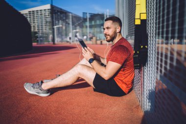 Ciddi bir adam antreman sırasında metal rendeleyerek oturup müzik listesinden şarkılar dinliyor.