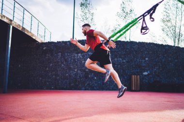 Stadyumda tek başına antrenman yaparken siyah şort giyen, direnç kayışlarıyla egzersiz yapan kararlı atletik erkek yan görünümü.