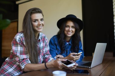 Kameraya gülümseyen bir proje üzerinde çalışırken, masa başında aletlerle oturan neşeli, genç bayan meslektaşlar.