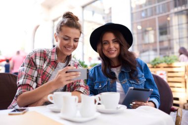 Günümüz modern kadınları kahve fincanları ve cep telefonlarıyla kafede oturuyorlar.