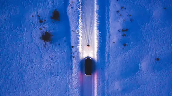 Aerial top view of car on rural area road while headlights are on in winter darkness, bird\'s eye view of suv vehicle in snowy north lands. Person standing front automobile which lighting the way